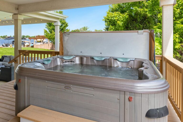 Explore a serene outdoor patio featuring a luxurious hot tub overlooking a tranquil lake.